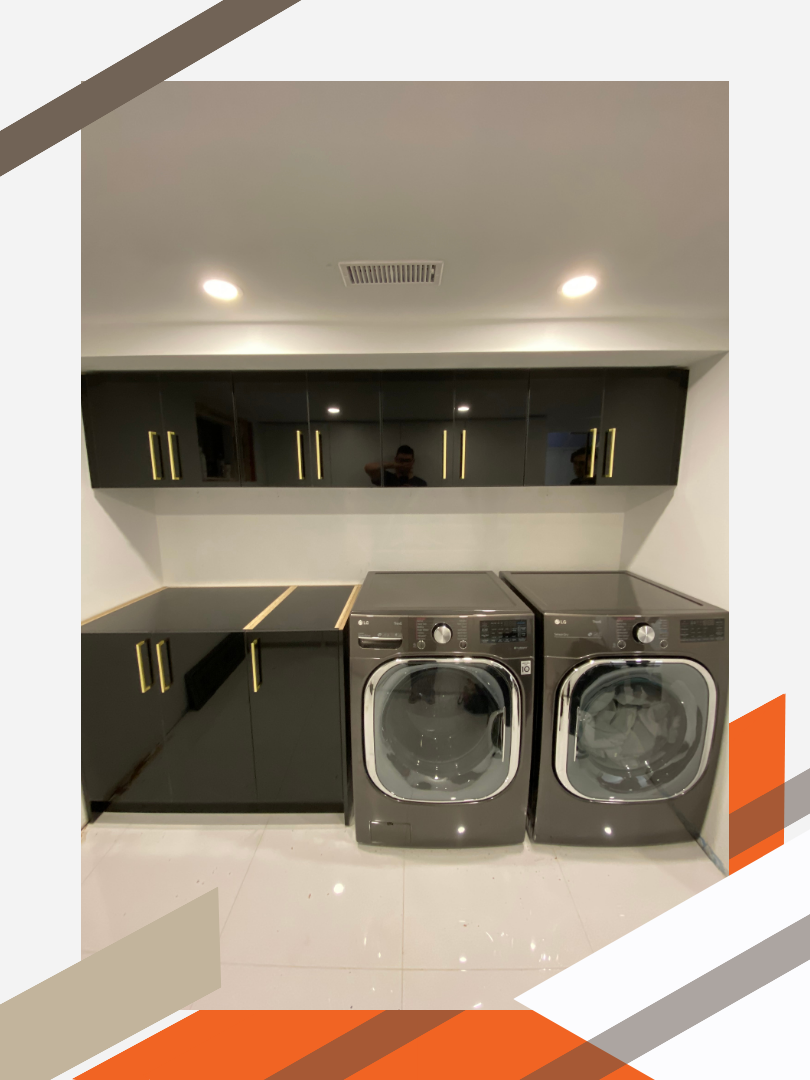 A well-lit, modern laundry room in a residential home. The cabinets are a sleek black colour with brass finishes.