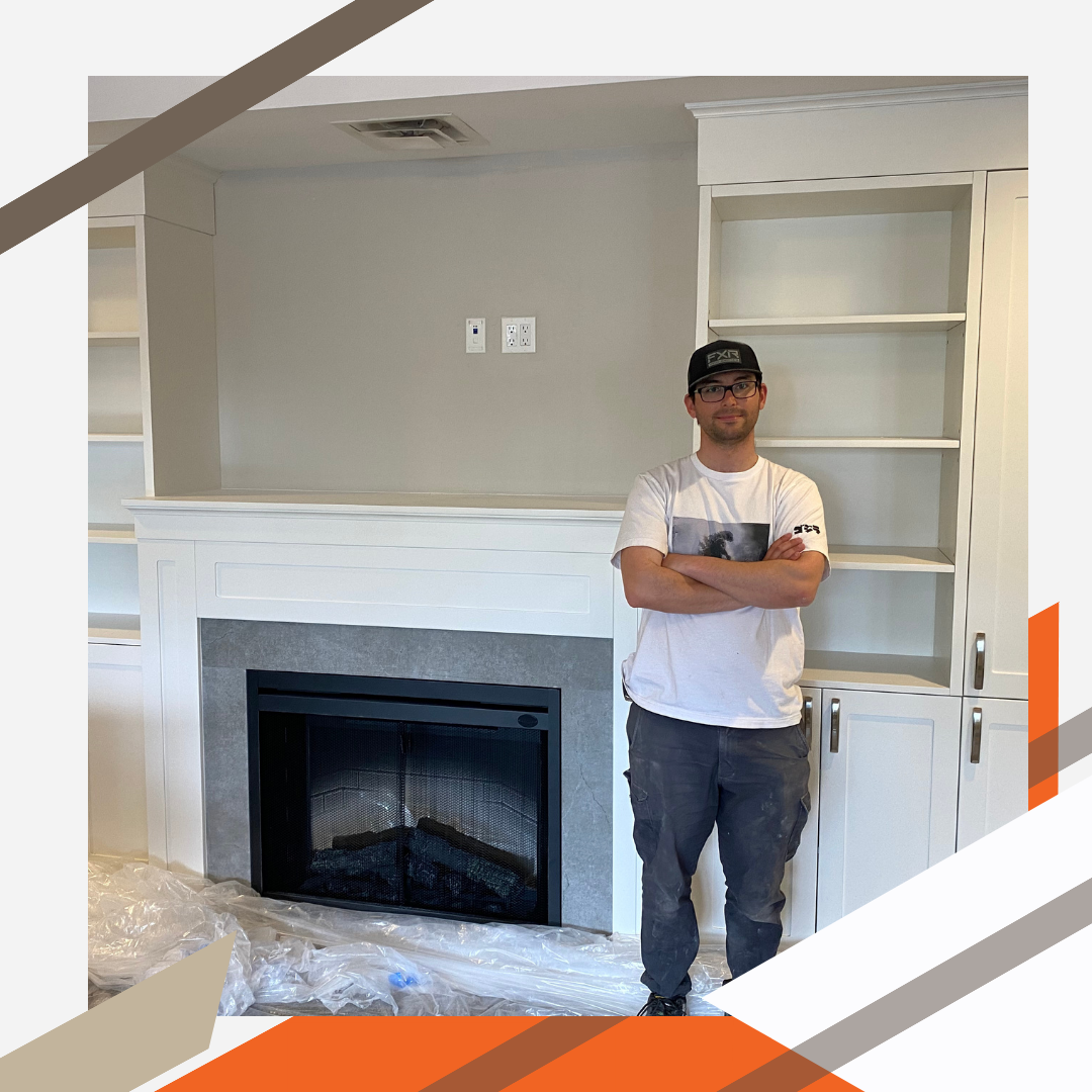 Skilled cabinet maker and company founder Tal Elyakim stands proudly in front of a newly installed set of cabinets and shelving. They provide clean and efficient storage space on either side of a modern fireplace.